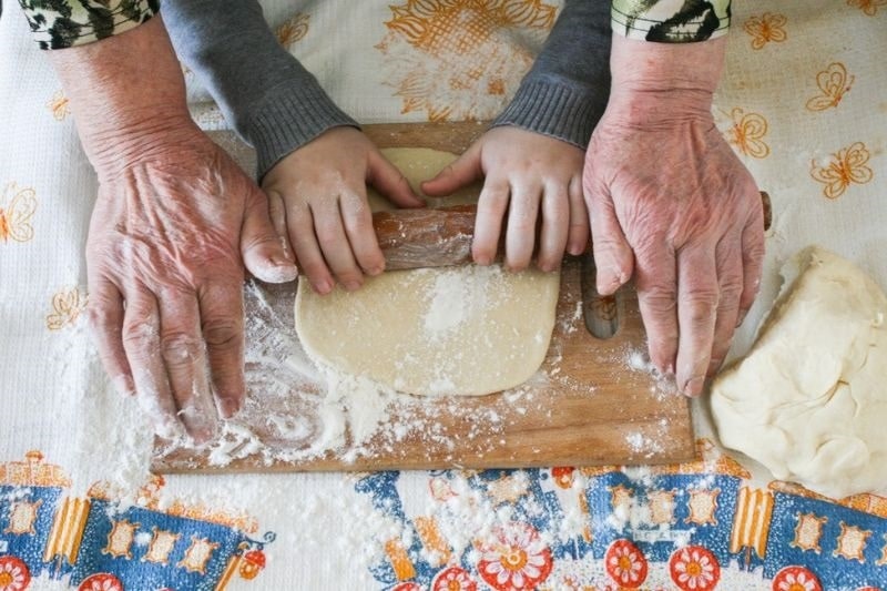 Mãos de uma avós e um neto fazendo massa de pão e usando. Imagem para ilustrar a matéria sobre avós e netos