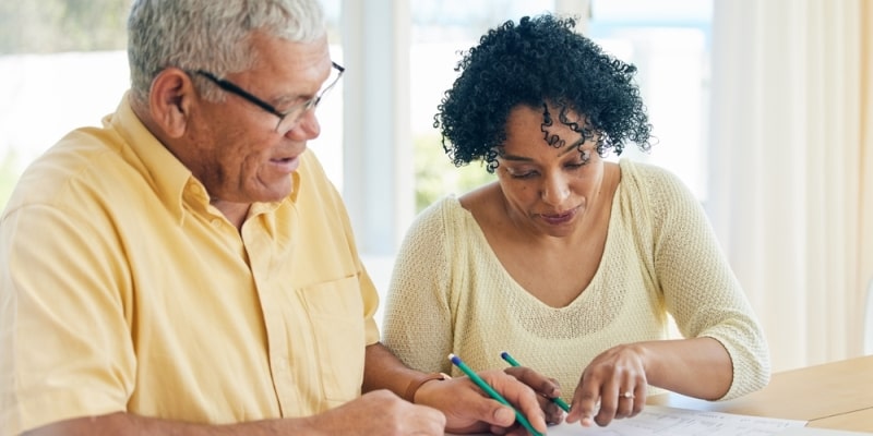 Um casal negro, de cerca de 50 anos, fazendo anotações em papéis de planejamento financeiro. Imagem para ilustrar a matéria de como fazer o dinheiro render mais.